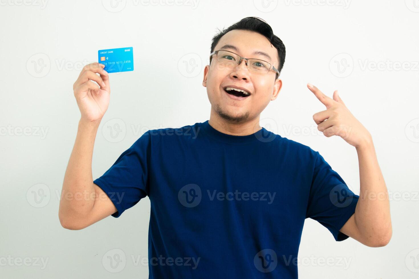 Smiling asian man blue tshirt hold and pointing credit card. Banking, Financial isolated background, blue color concept. photo