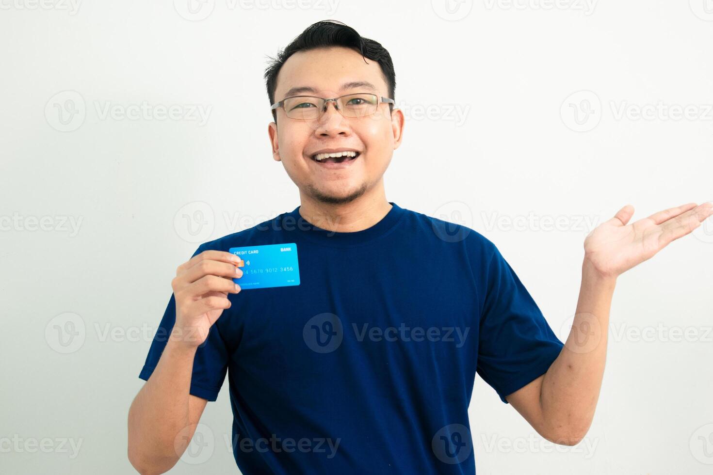 Cheerful asian man hold credit card and showing gesture. Banking, Financial isolated background, blue color concept. photo