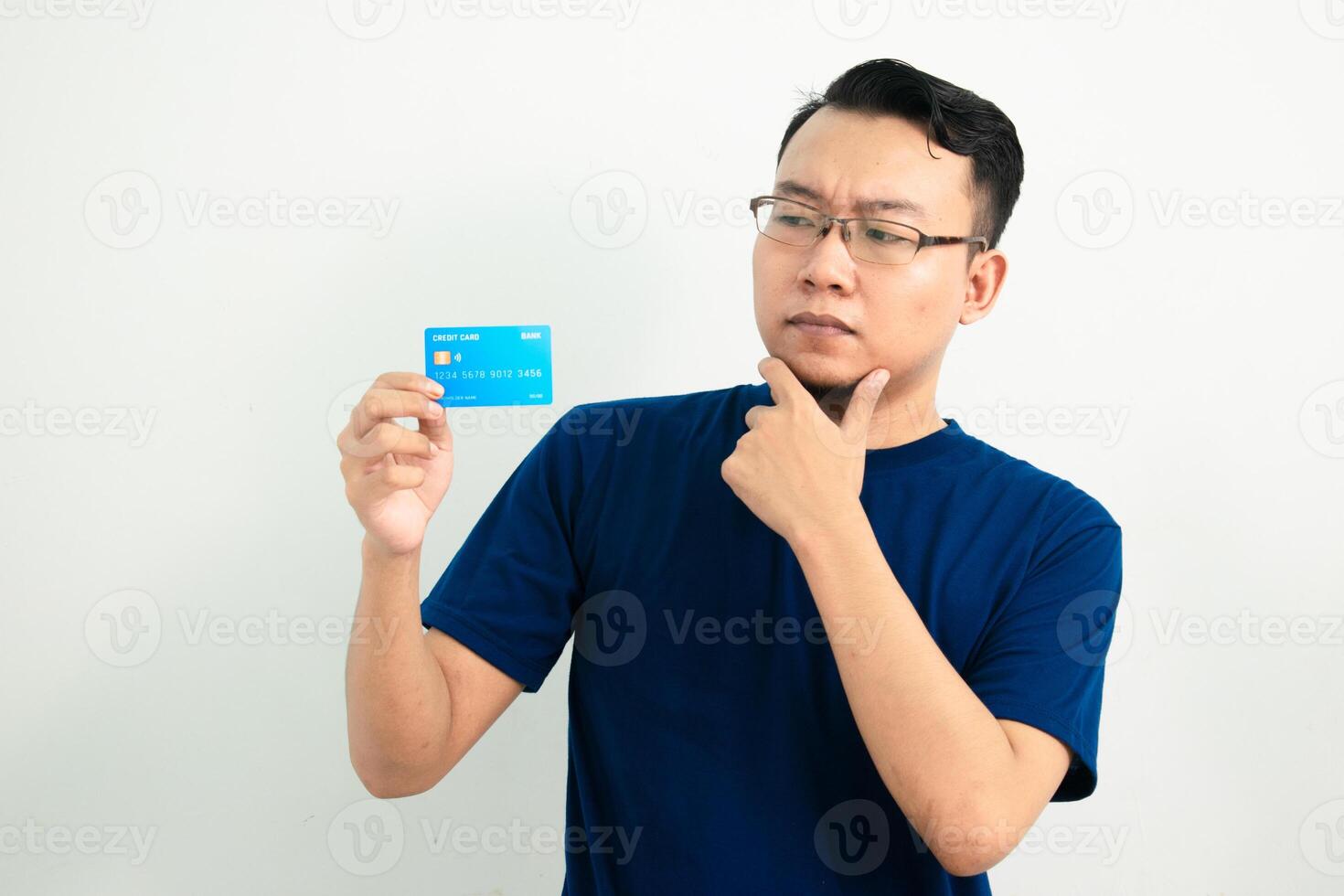 Thoughtful asian man hold and pointing credit card. Banking, Financial isolated background, blue color concept. photo