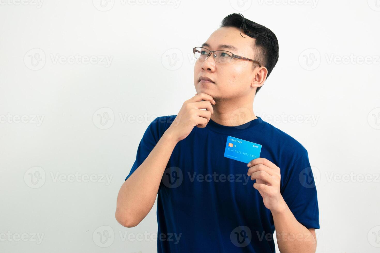 Thinking asian man hold and pointing credit card. Banking, Financial isolated background, blue color concept. photo