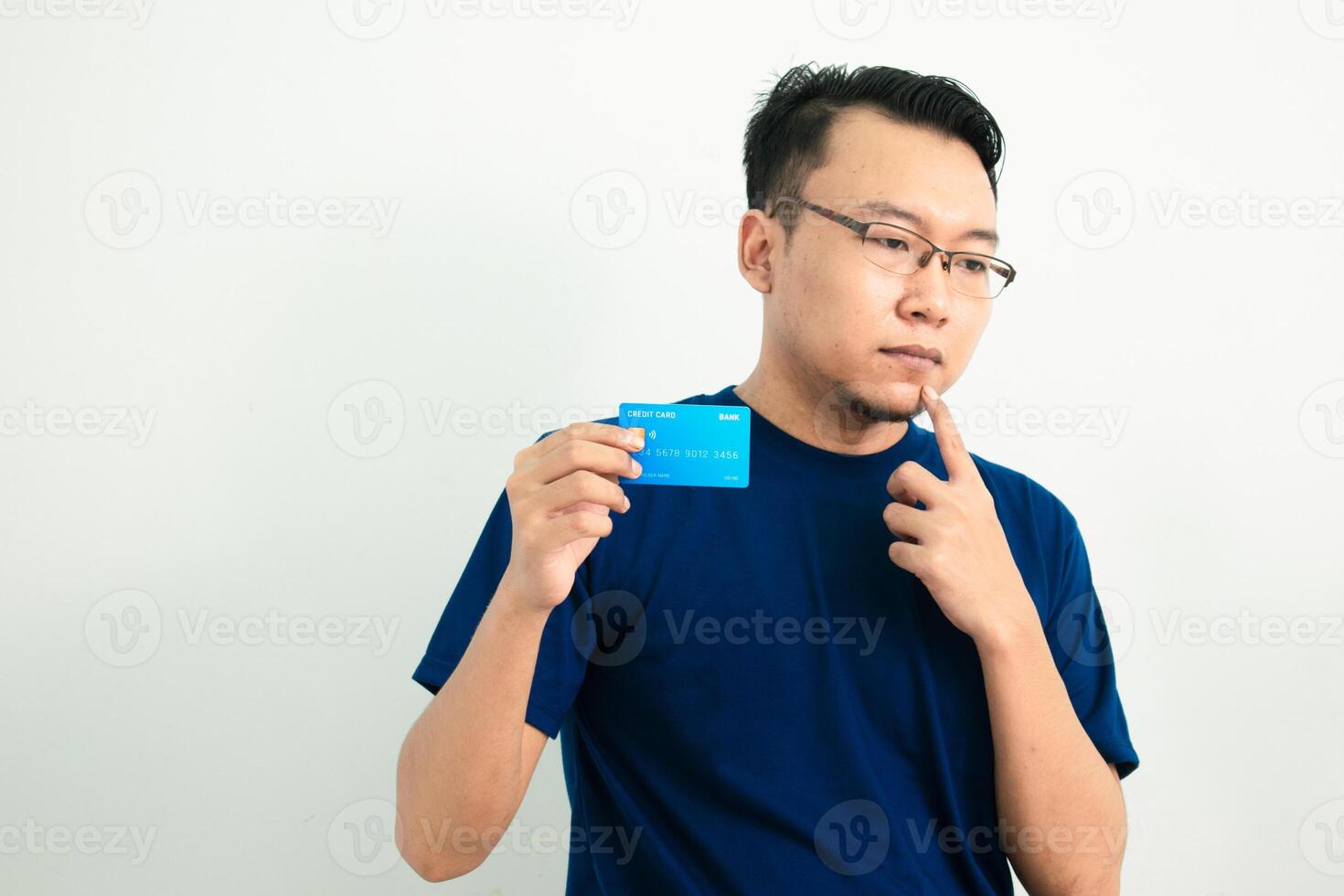 Thoughtful asian man blue tshirt hold and pointing credit card. Banking, Financial isolated background, blue color concept. photo