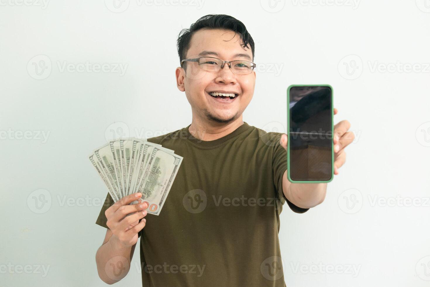 Delighted asian man hold Money and showing phone screen. Banking, Financial and technology isolated background, green color concept. photo