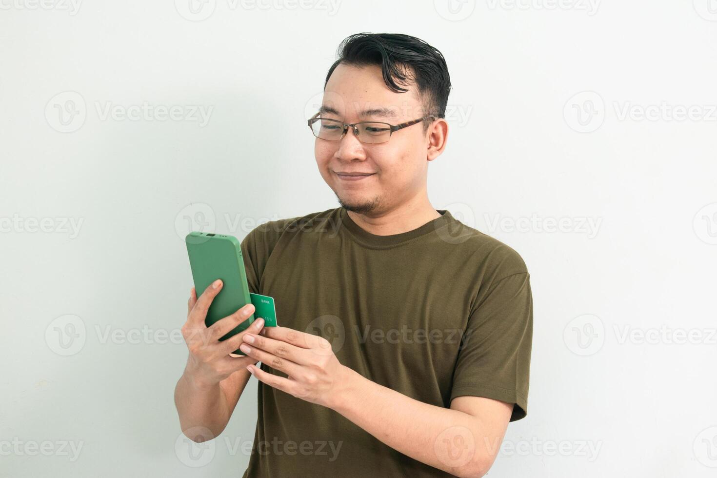 Happy Asian man doing transaction with credit card and phone. Banking, Financial and technology isolated background, green color concept. photo