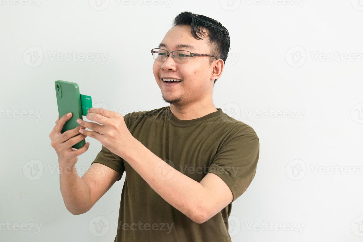 Joyful Asian man doing transaction with credit card and phone. Banking, Financial and technology isolated background, green color concept. photo