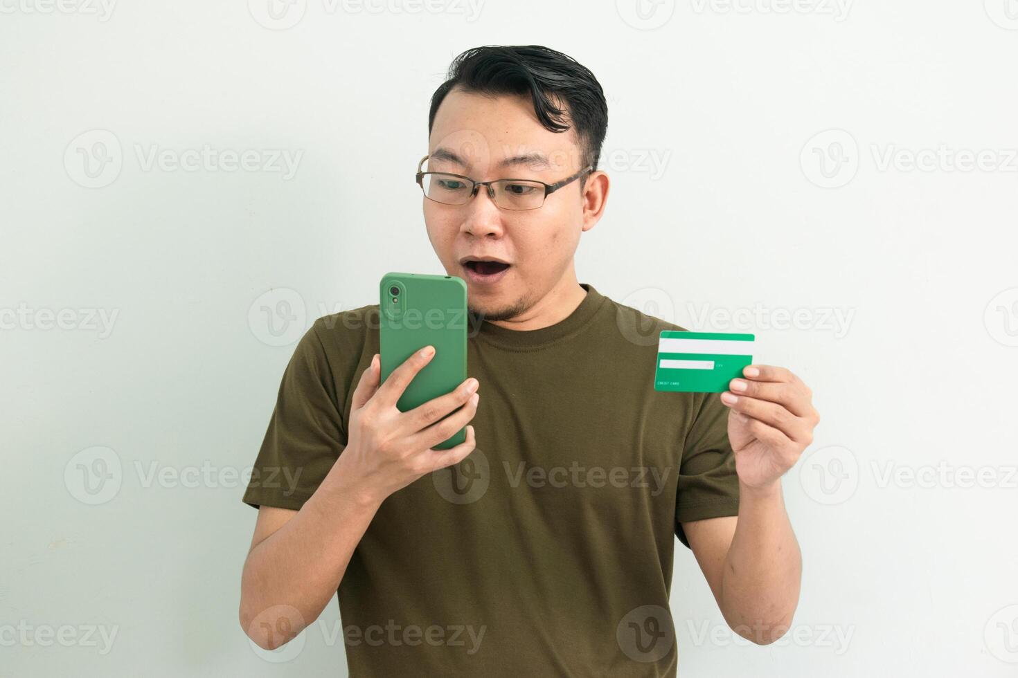 Shocked Asian man doing transaction with credit card and phone. Banking, Financial and technology isolated background, green color concept. photo