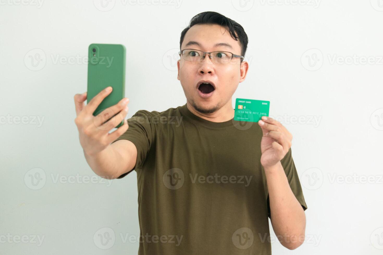 Surprised Asian man wear green tshirt doing transaction with credit card and phone. Banking, Financial and technology isolated background photo