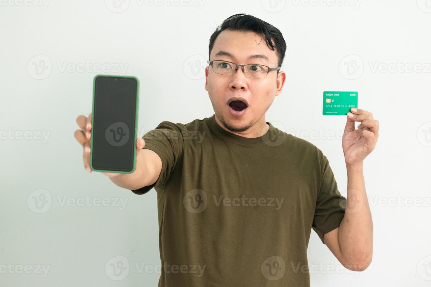 Surprised Asian man wear green tshirt doing transaction with credit card and phone. Banking, Financial and technology isolated concept. photo
