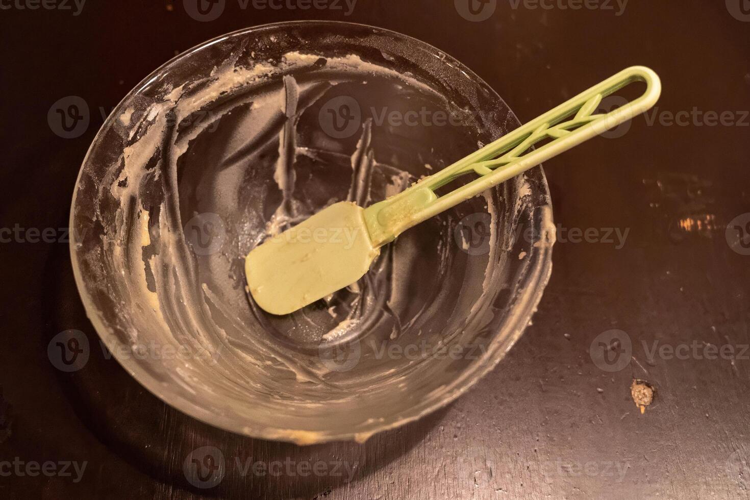 Empty mixing bowl with spatula resting on dark wooden table photo