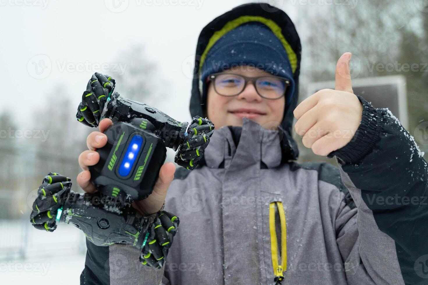 Boy showing thumb up while holding transforming robot car toy in snowy park photo