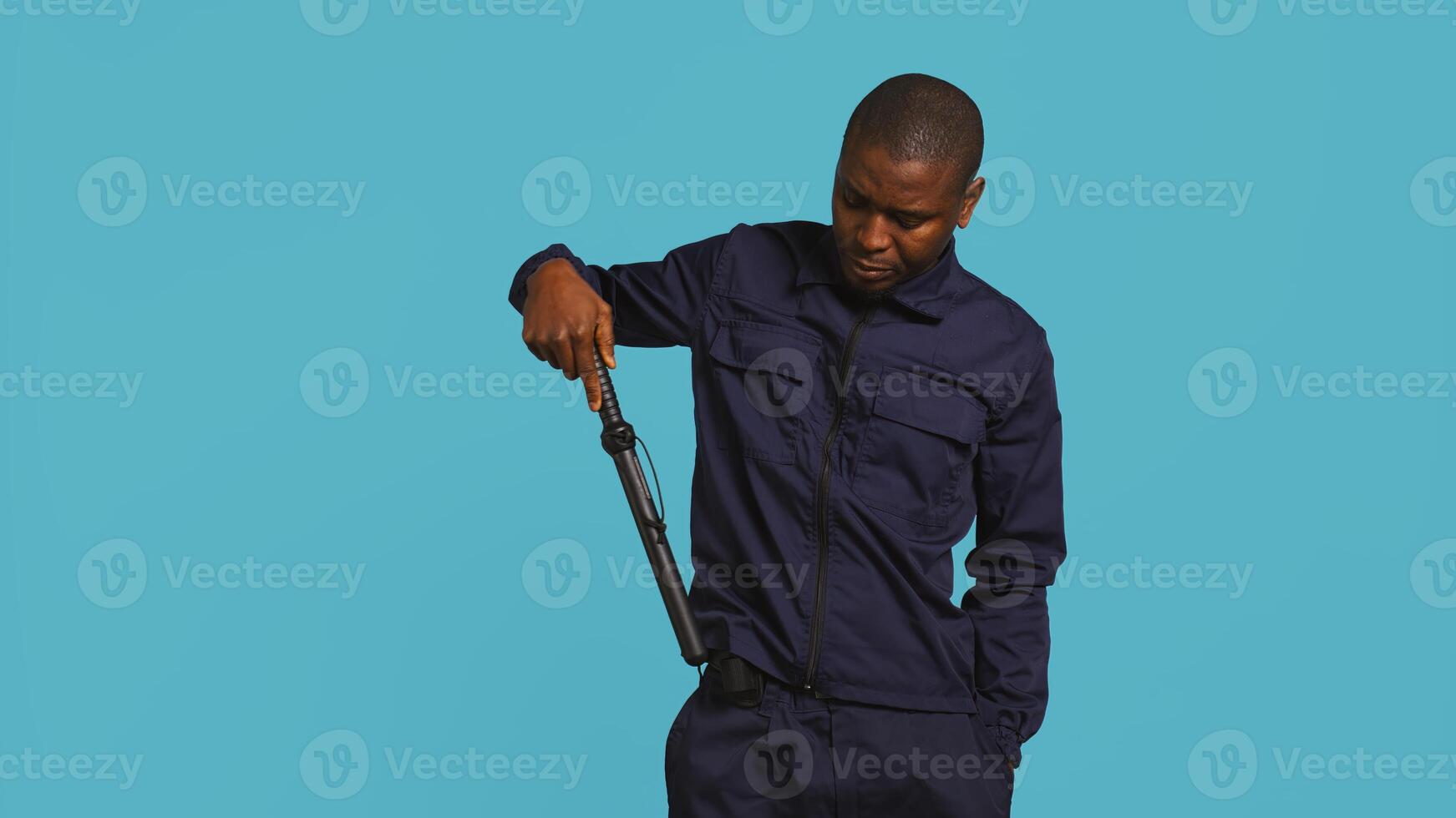 Portrait of security agent removing baton from belt, using it to secure assigned post, studio background. African american guardian pointing finger to truncheon, handling security breaches, camera B photo