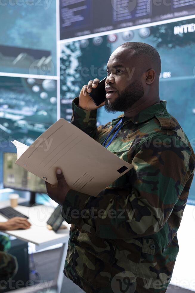 High tech military man discuss on phone call about crucial information, soldier analyzing real time data and processing intelligence. Support military missions effectively for safety. photo