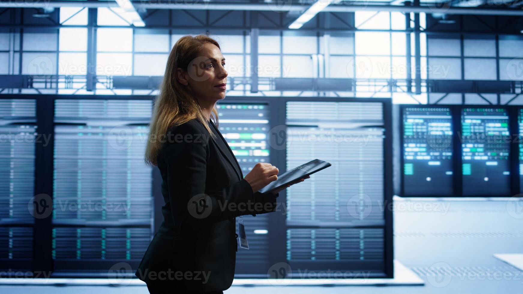 Engineer in server hub checking recovery plan on tablet, monitoring rackmounts energy consumption. Woman in data center making sure rigs are functioning optimally, doing routine disk checks, camera B photo