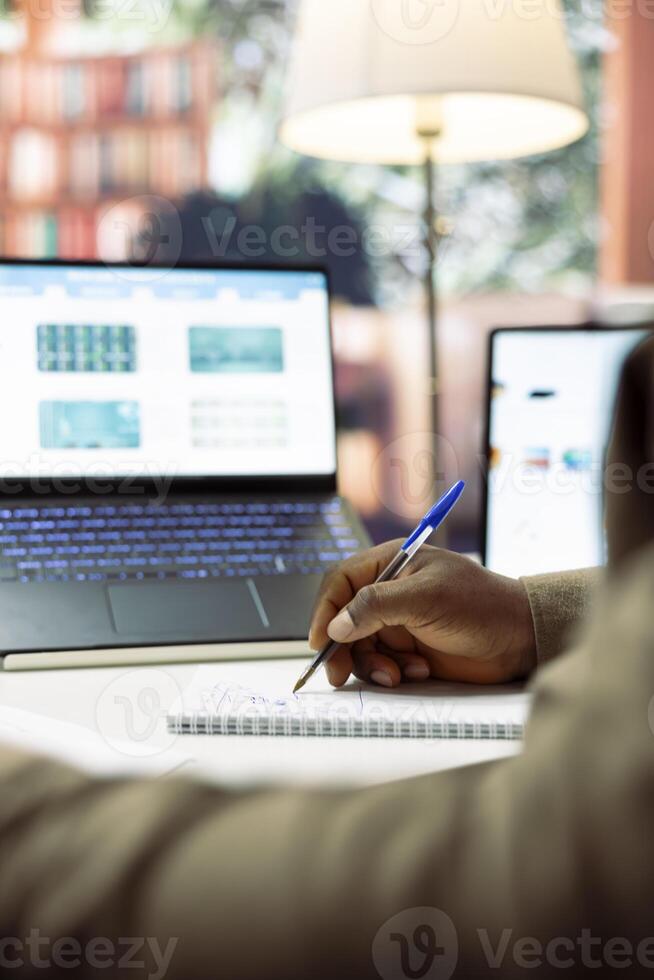 Businessman calculates monthly accounting balance on a notebook, studying financial reports and sales data at home desk. Entrepreneur reviewing business progress numbers. Close up. photo