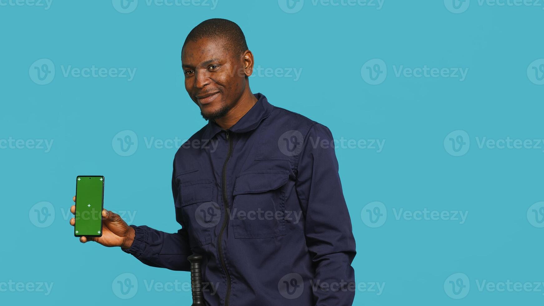Smiling security guard working protection job presenting mockup smartphone, studio backdrop. Portrait of upbeat bodyguard showcasing green screen phone, isolated over studio background photo