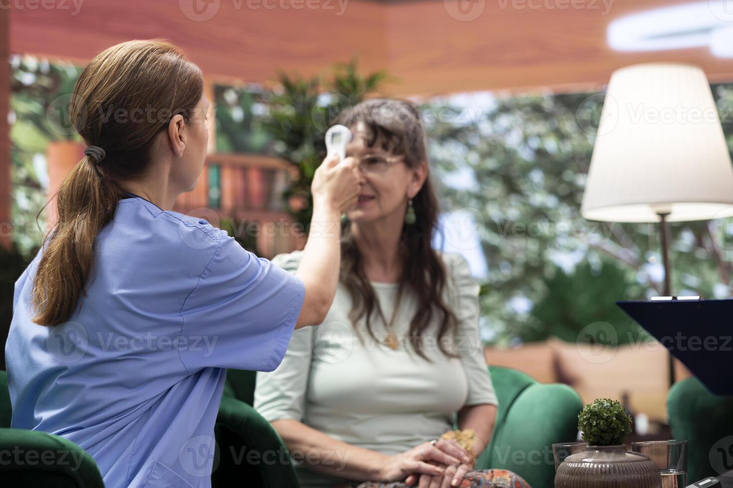 Medical caregiver uses thermometer on senior patients to check temperature, fever measurement during consultation at home checkup. Nurse visiting old people for support and health aid. photo