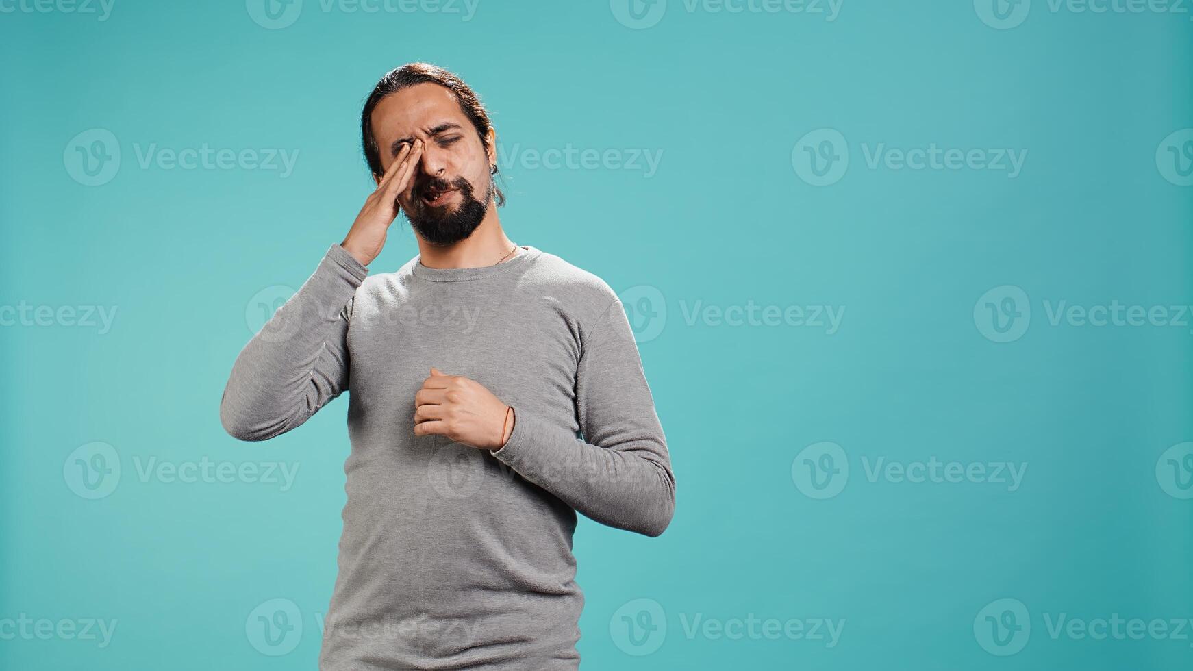 Man feeling exhausted from overworking and lack of sleep, rubbing eyes and yawning, isolated over studio background. Tired person feeling sleepy, being fatigued, studio backdrop, camera B photo