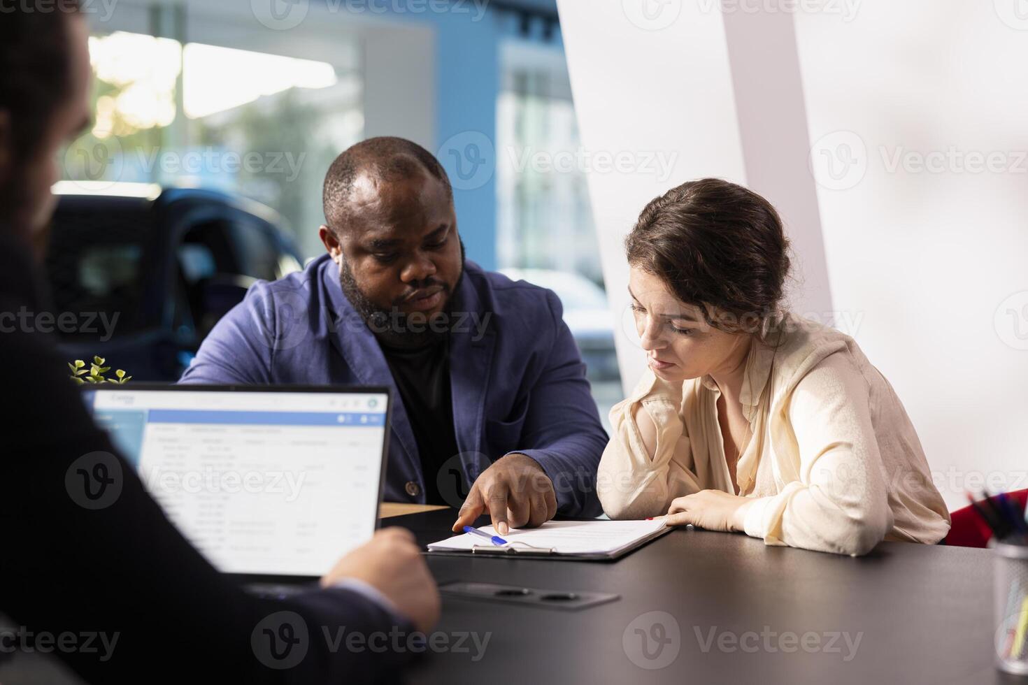 Customers in showroom completing credit application and financing paperwork after deciding to purchase new car. Salesman in dealership discussing financing options with clients photo