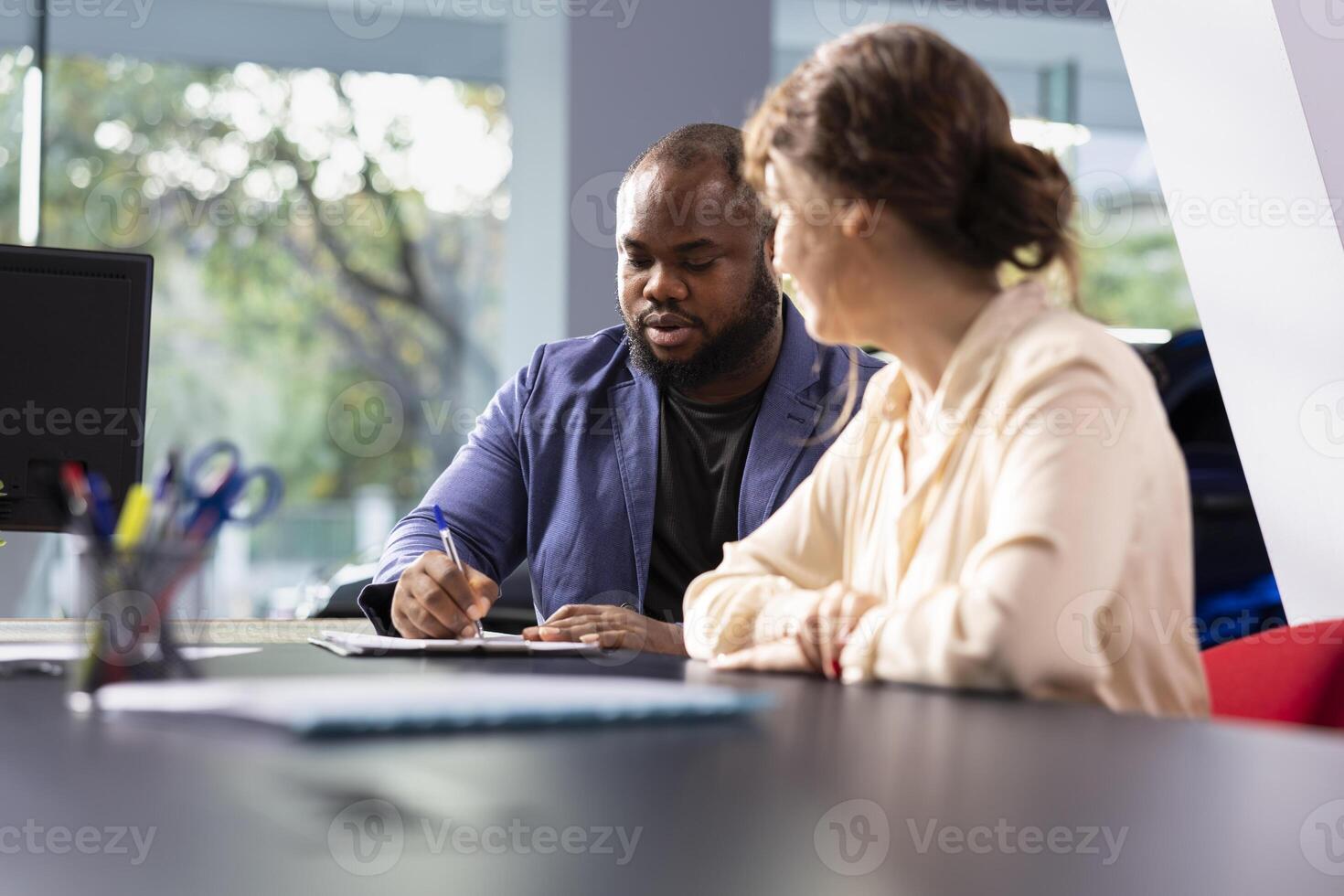 Clients signing contract after being shown dealership vehicles by car salesperson explaining features and warranties. Customers completing forms after comparing car models and choosing automobile photo