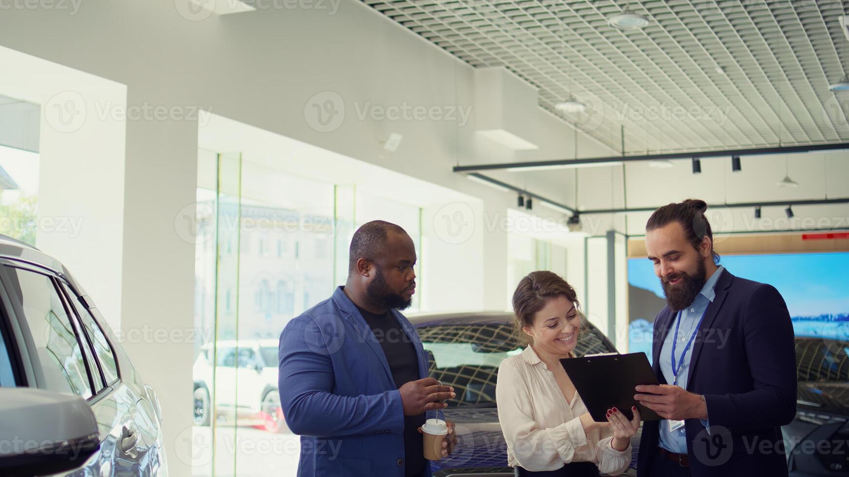 Car dealership salesman giving sale contract for satisfied clients to sign after conducting test drive. Showroom agent suggesting clients extra features to buy, asking for signature, camera B photo