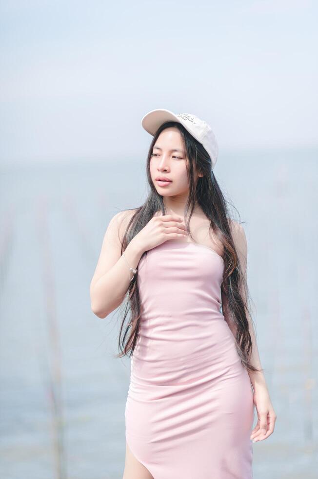A woman in a pink dress and hat standing by the water photo