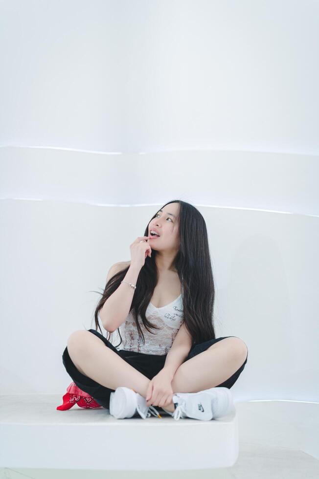 A woman sitting on a white wall with her hand on her mouth photo