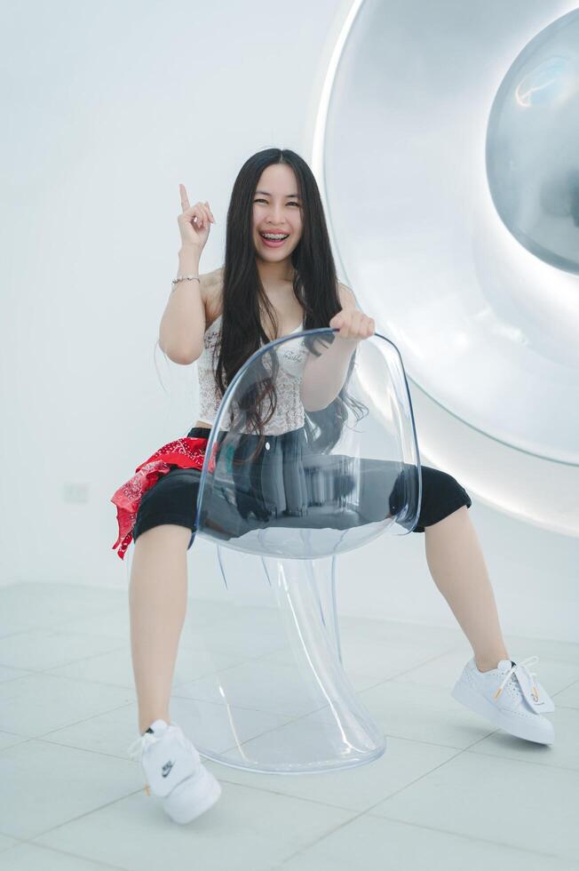 Happy Young Woman Sitting on Transparent Chair in Modern Interior photo