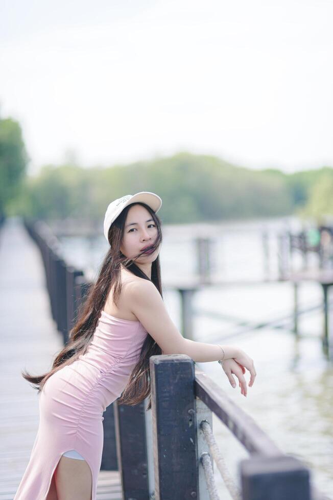 A woman in a pink dress leaning on a wooden bridge photo
