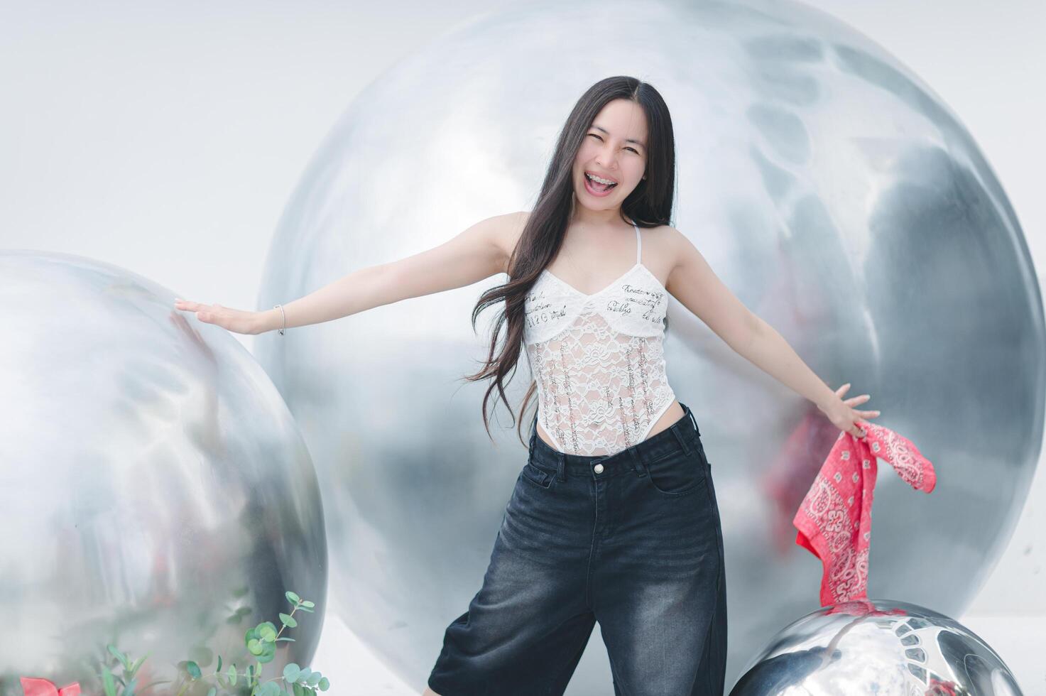 A woman in a white top and jeans is standing next to a large silver ball photo