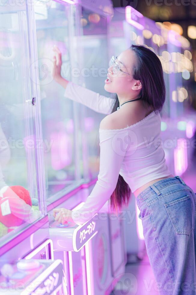 Young Woman Engaging with Colorful Claw Machine in Neon Arcade photo