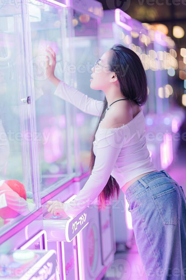 Young Woman Enjoying Claw Machine in Neon Arcade Setting photo