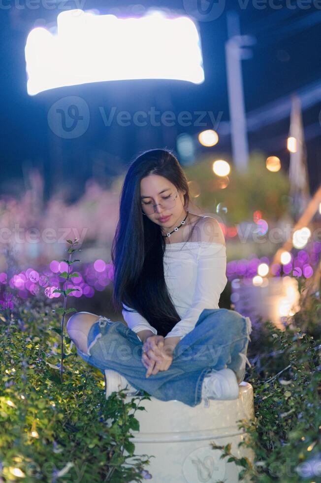 Young Woman Sitting Cross-Legged in Urban Night Scene with Lights photo