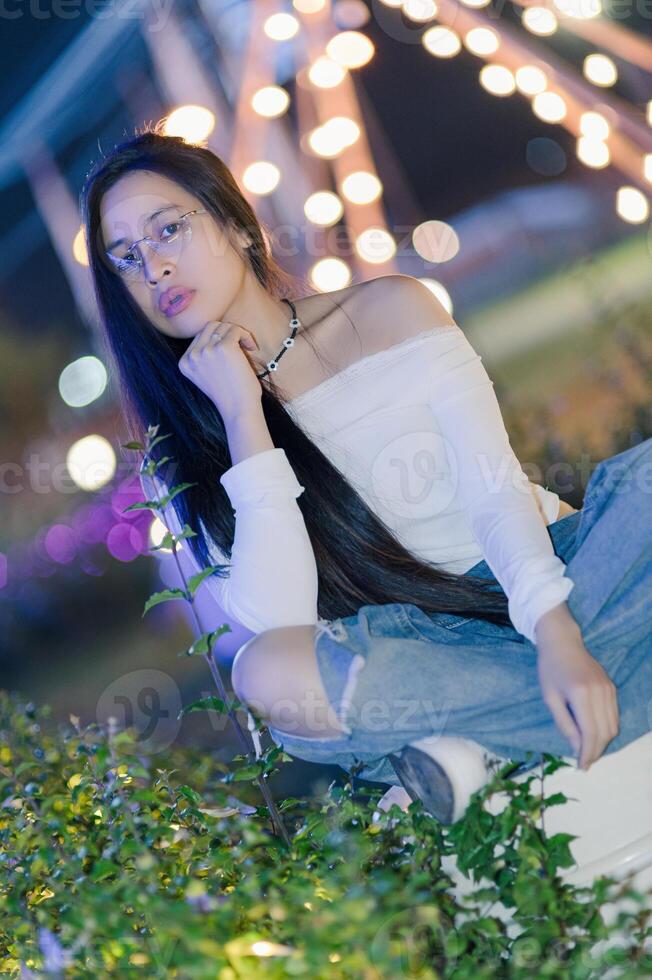 Young Woman Posing Outdoors at Night Surrounded by Colorful Lights photo