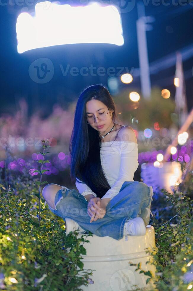 Young Woman Sitting on Barrel Surrounded by Colorful Lights at Night photo