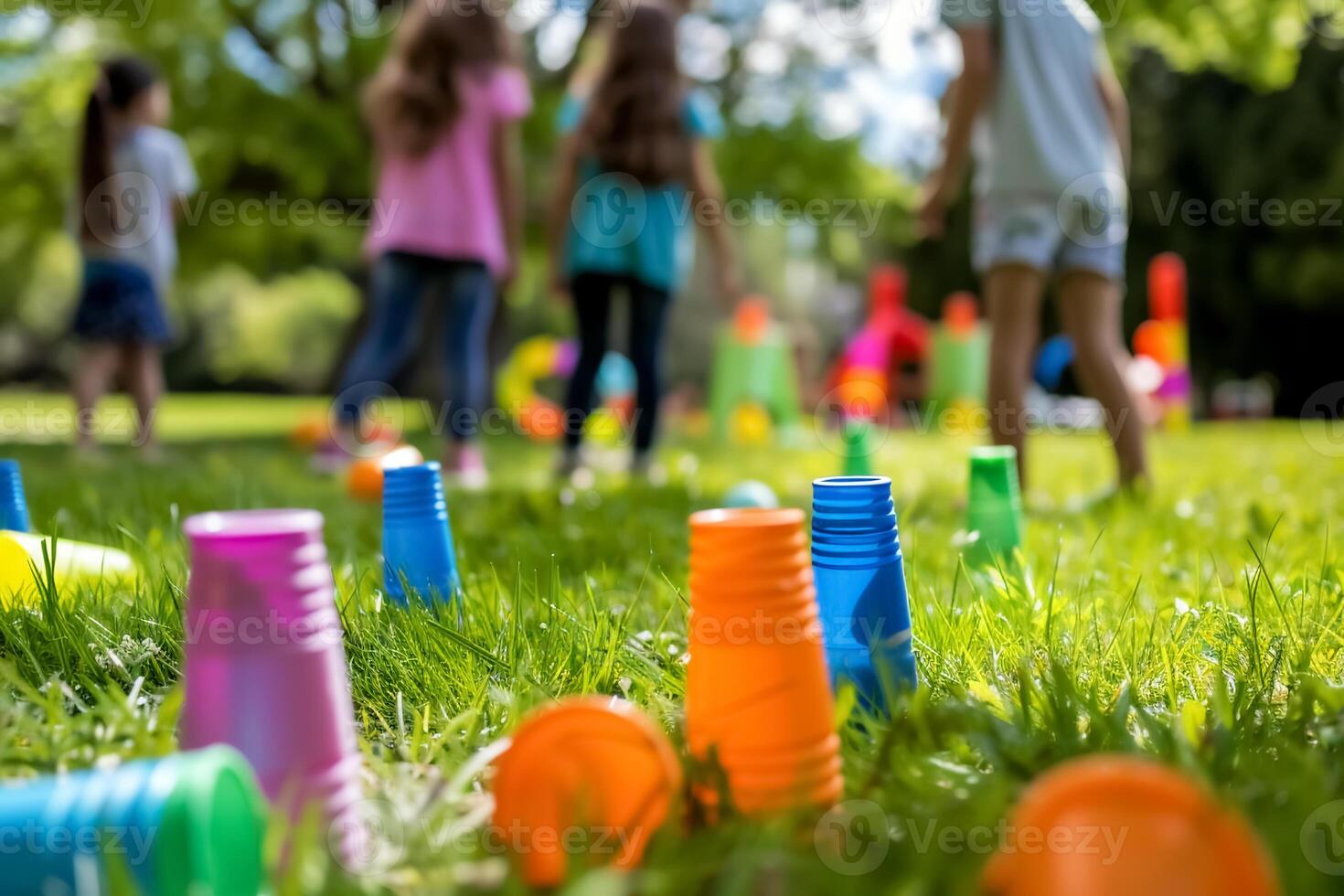 Colorful plastic cups scattered on grass with children playing in background, enjoying sunny day outdoors photo