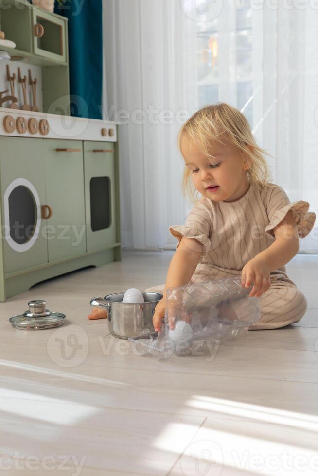 Child playing with white eggs and kitchen utensils on a wooden floor during morning hours photo