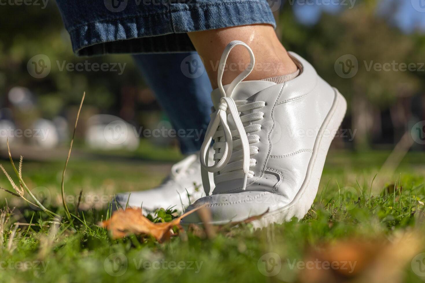 A person steps carefully on lush green grass while wearing white sneakers. photo