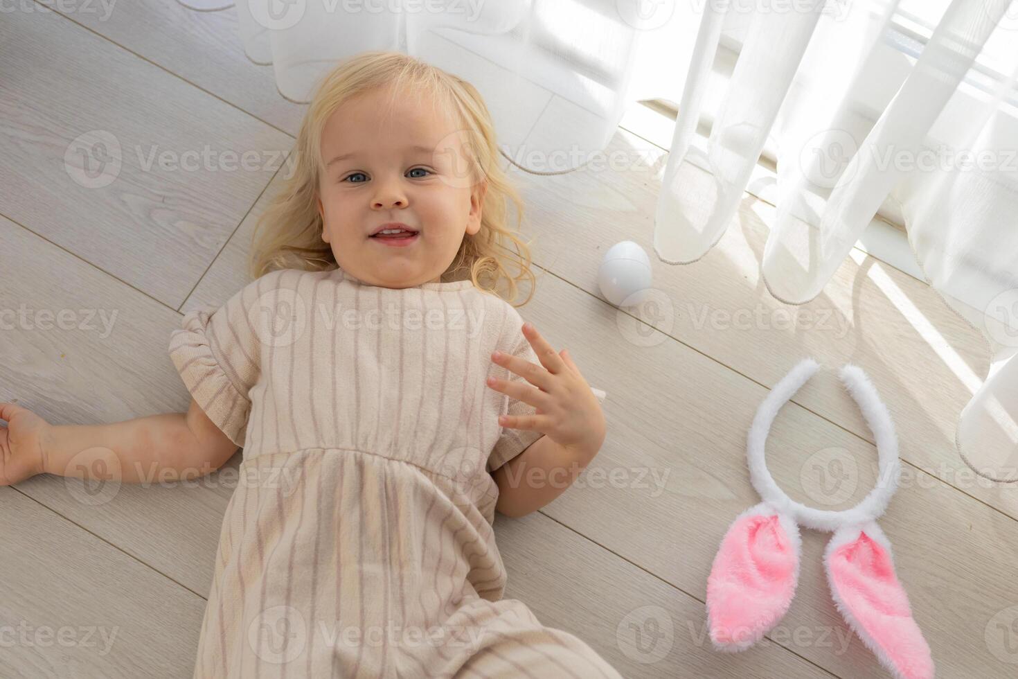 Child lying on the floor with bunny ears and colorful eggs during a playful holiday celebration photo