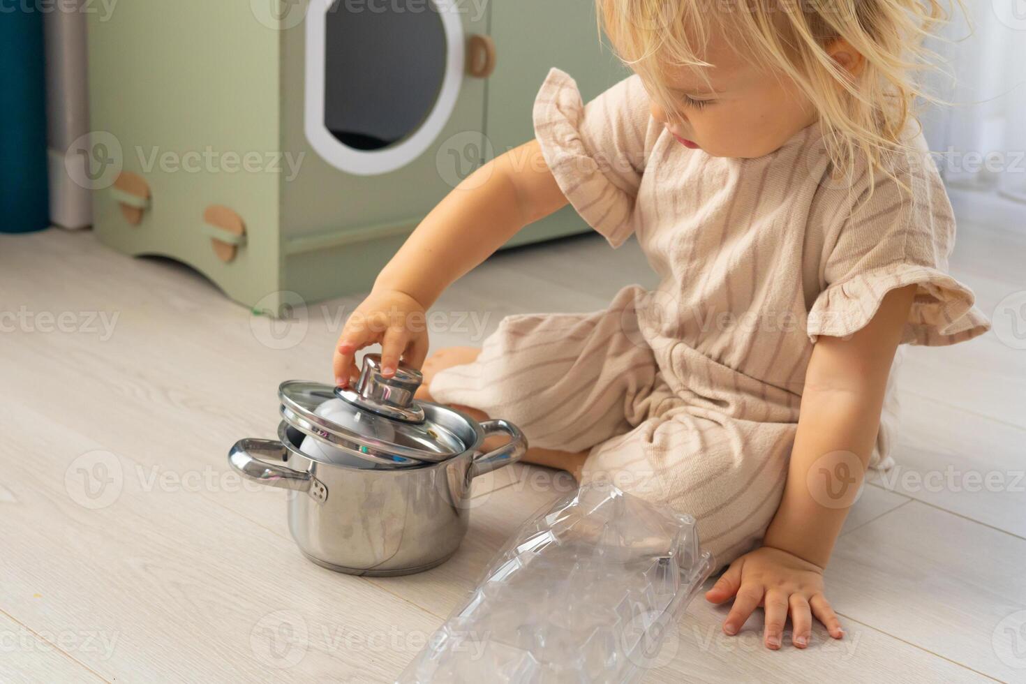Child playing with white eggs and kitchen utensils on a wooden floor during morning hours photo