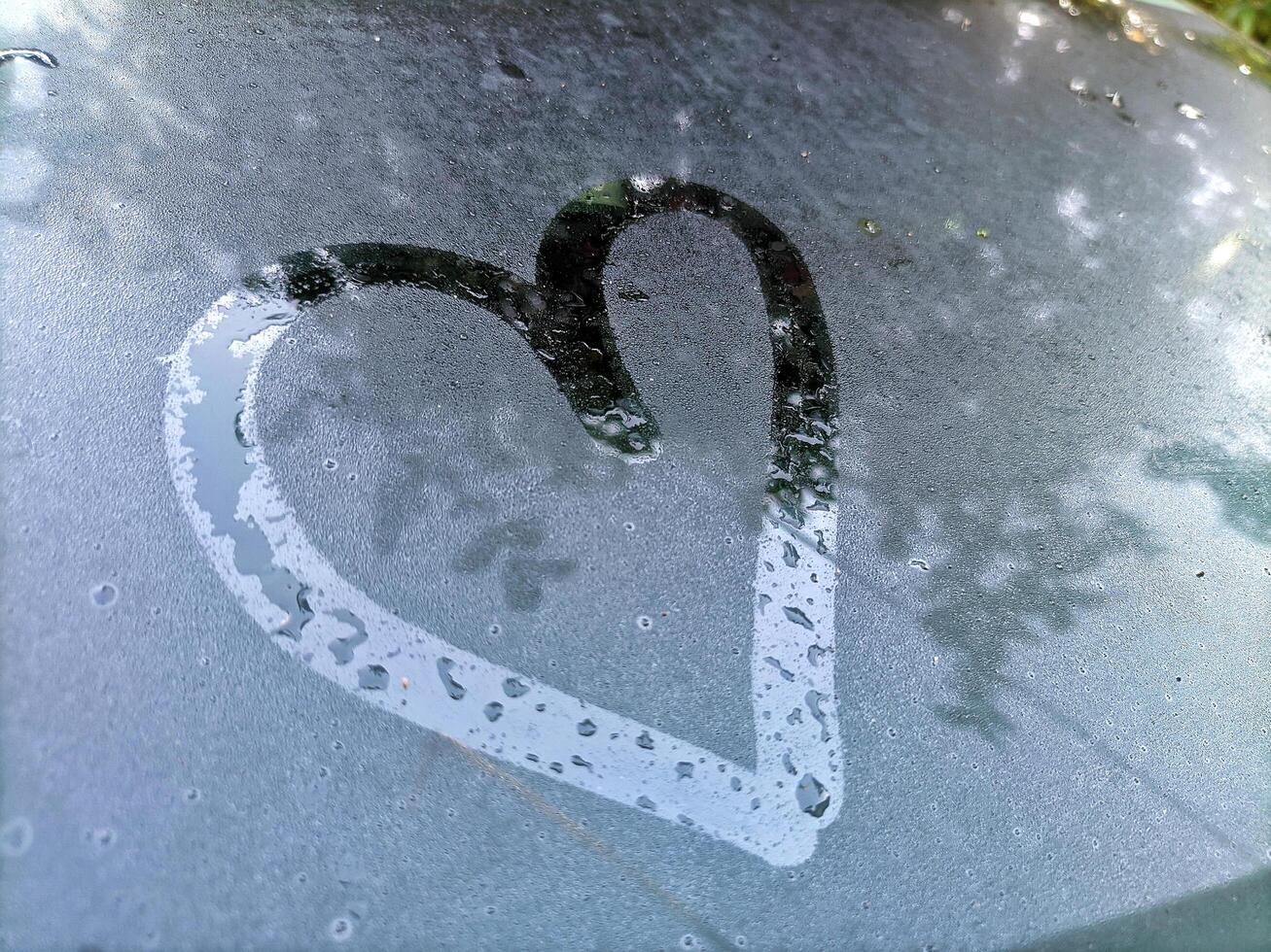 Selective focus of Love symbol on wet car window or dew. Autumn rain photo