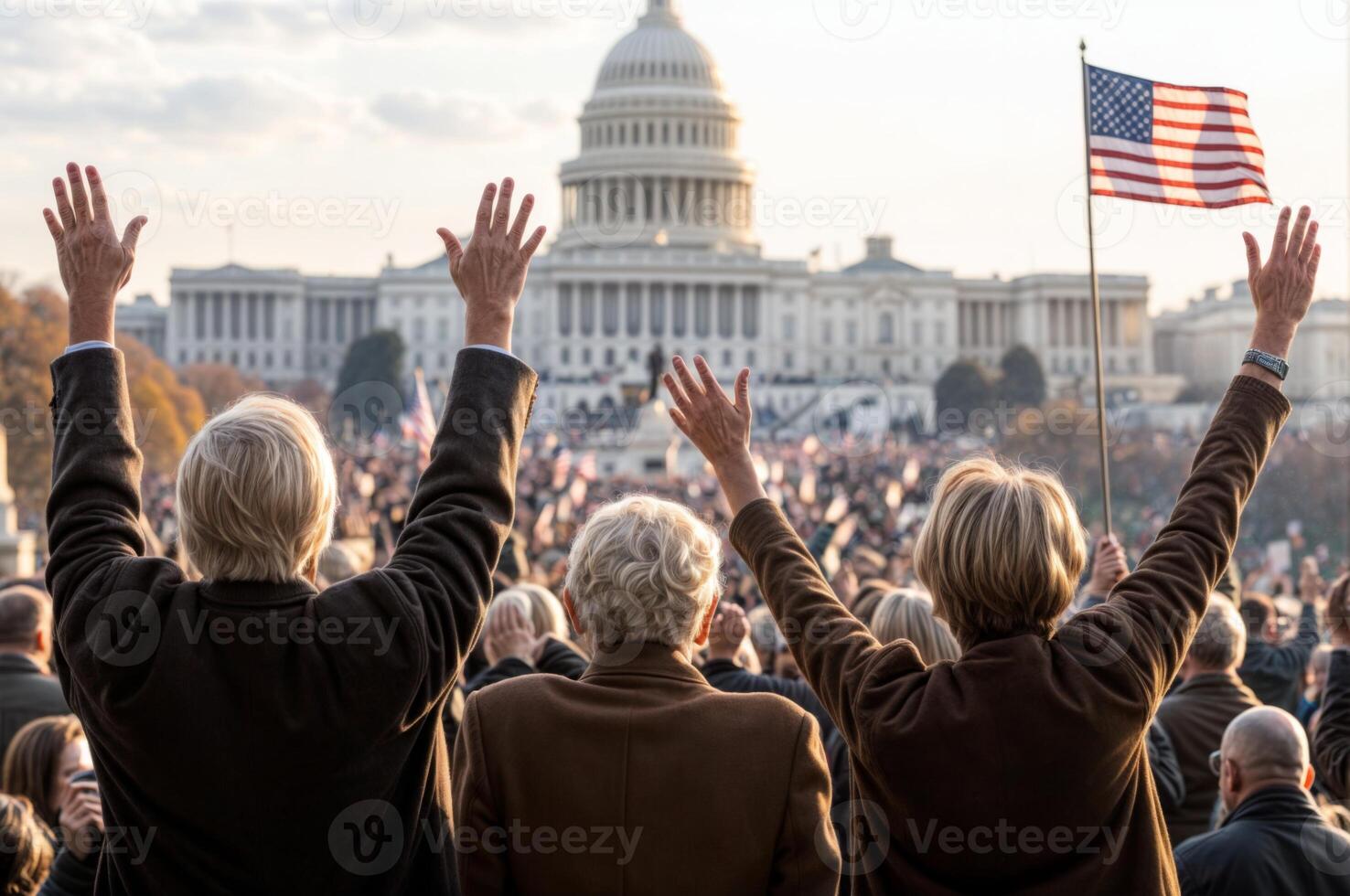 Crowd celebrates at inauguration near iconic Capitol building with American flags waving in the early light. Raised hands photo