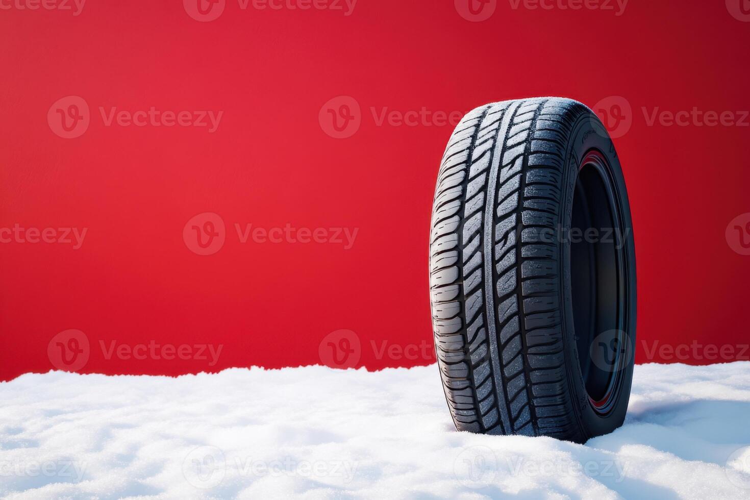 Tire resting on snow against a bold red backdrop showcasing winter readiness and performance photo