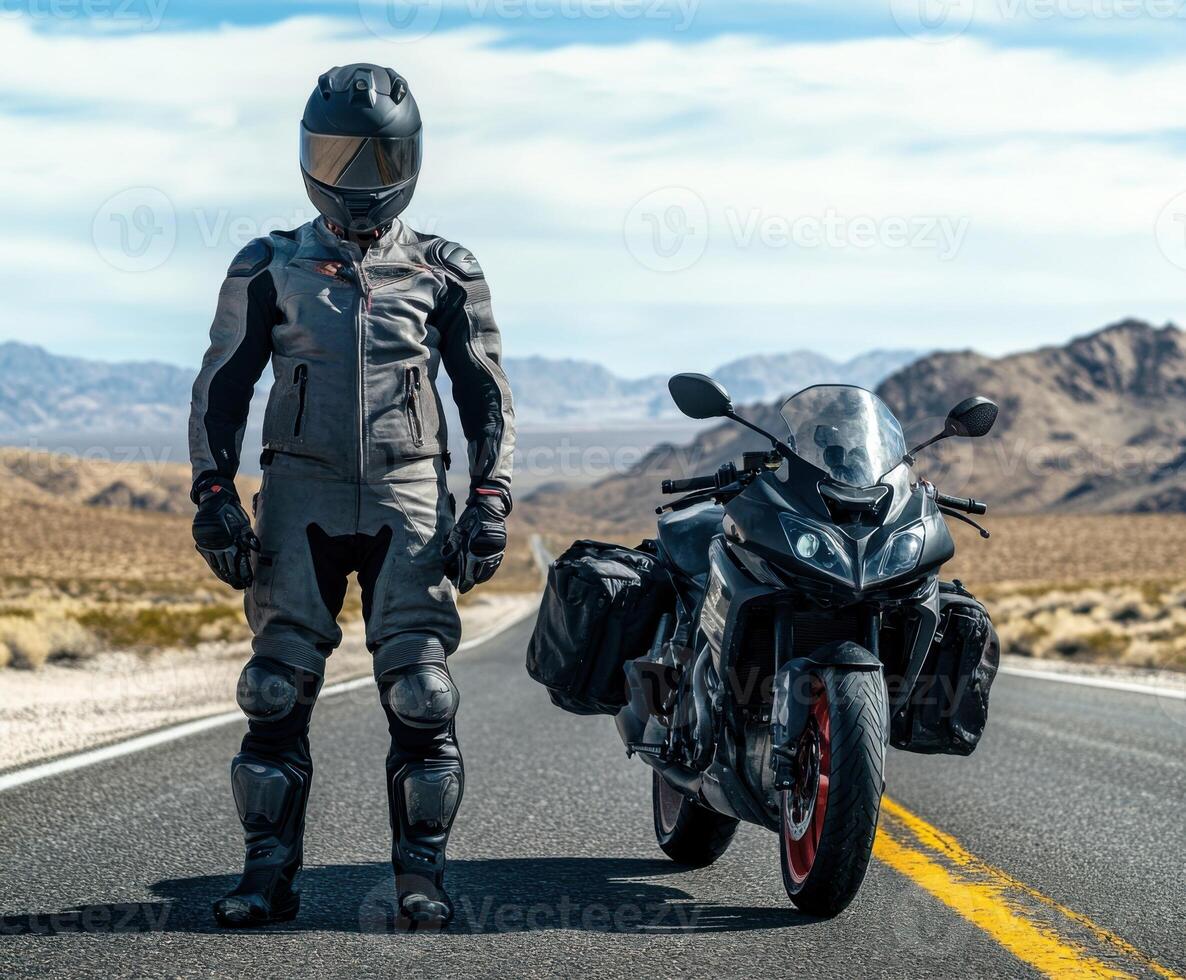Motorcyclist in leather suit stands confidently beside sportbike on open road in desert landscape photo