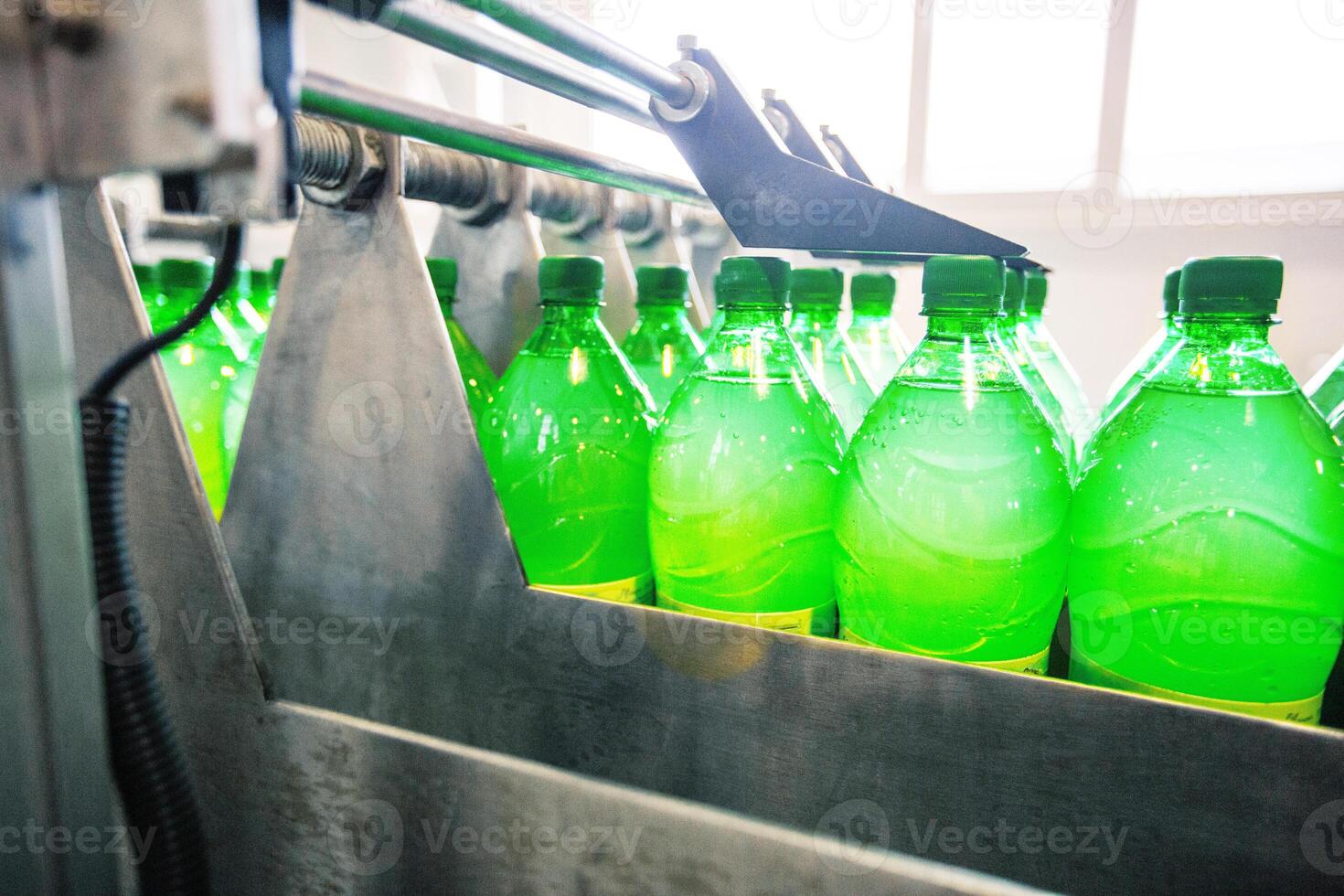 Bottles filled with green liquid move through a production line at a beverage manufacturing facility in the afternoon photo