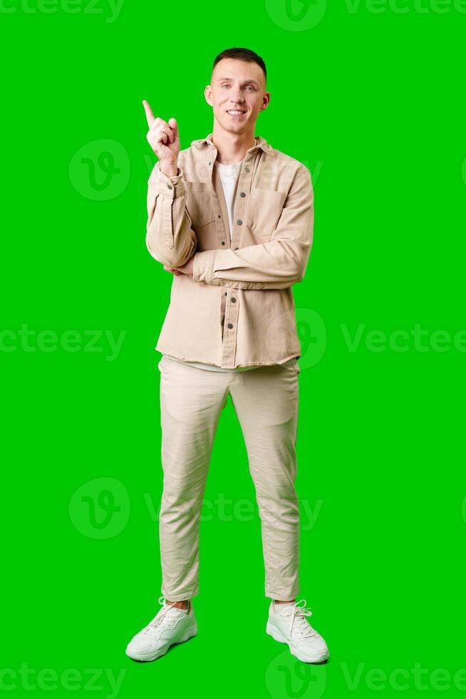 Young Man Pointing Upward While Smiling Against a Bright Green Background photo