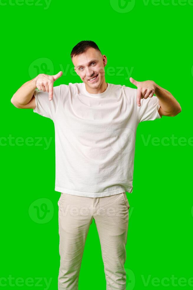 Young Man in a White Shirt Pointing Downward Against a Bright Green Background photo