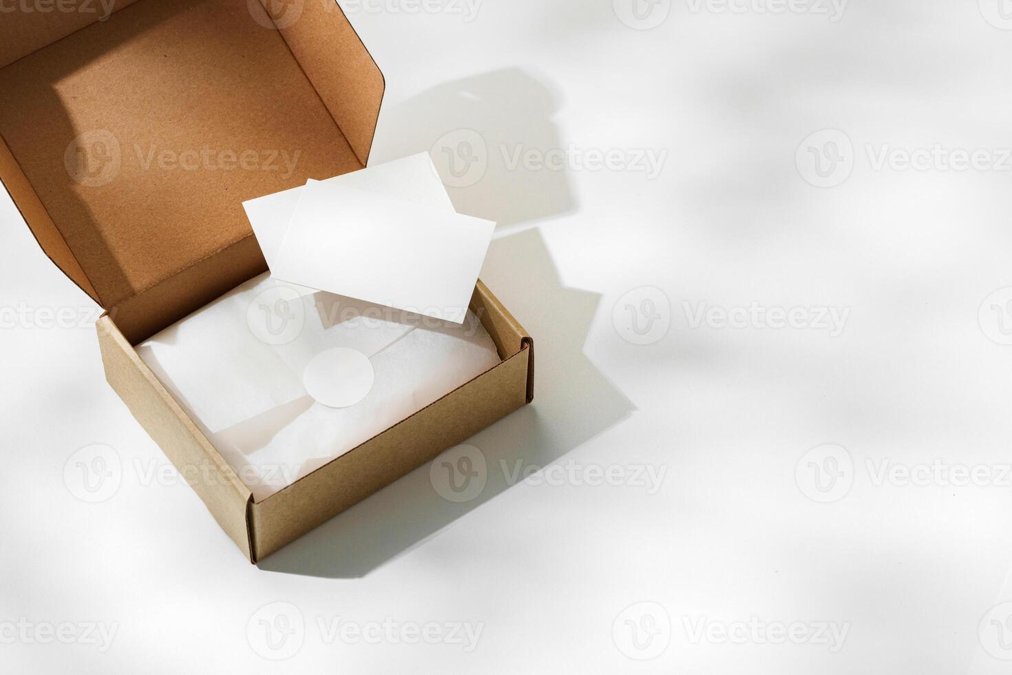 Brown cardboard box with a blank envelope on a light background in a well-lit setting photo