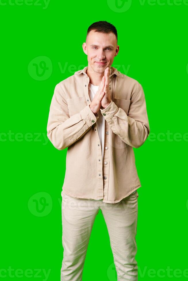 Young Man Wearing Beige Jacket and Pants Standing With Hands Together Against Bright Green Background photo