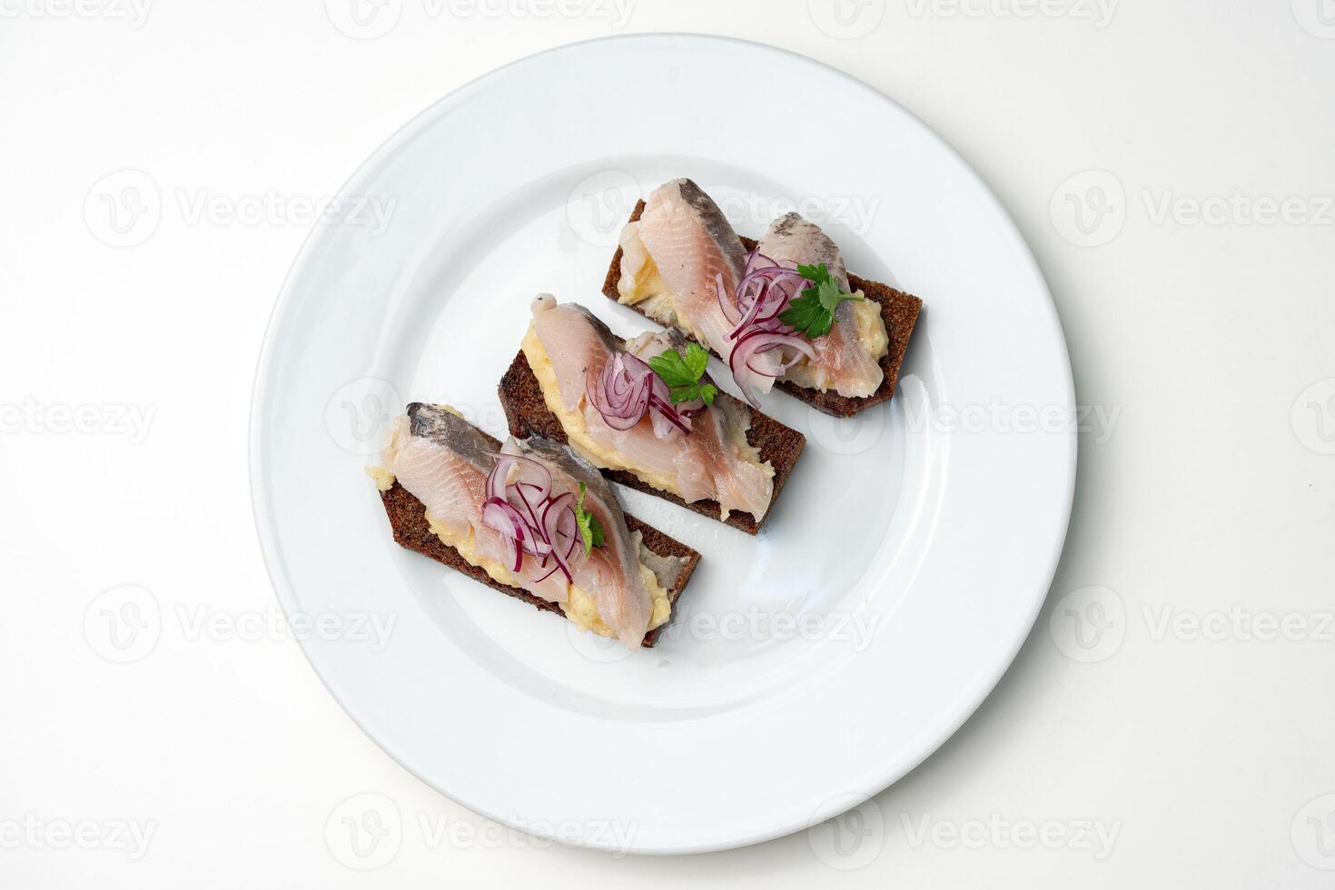 Open-faced sandwiches with herring and onions served on a white plate photo