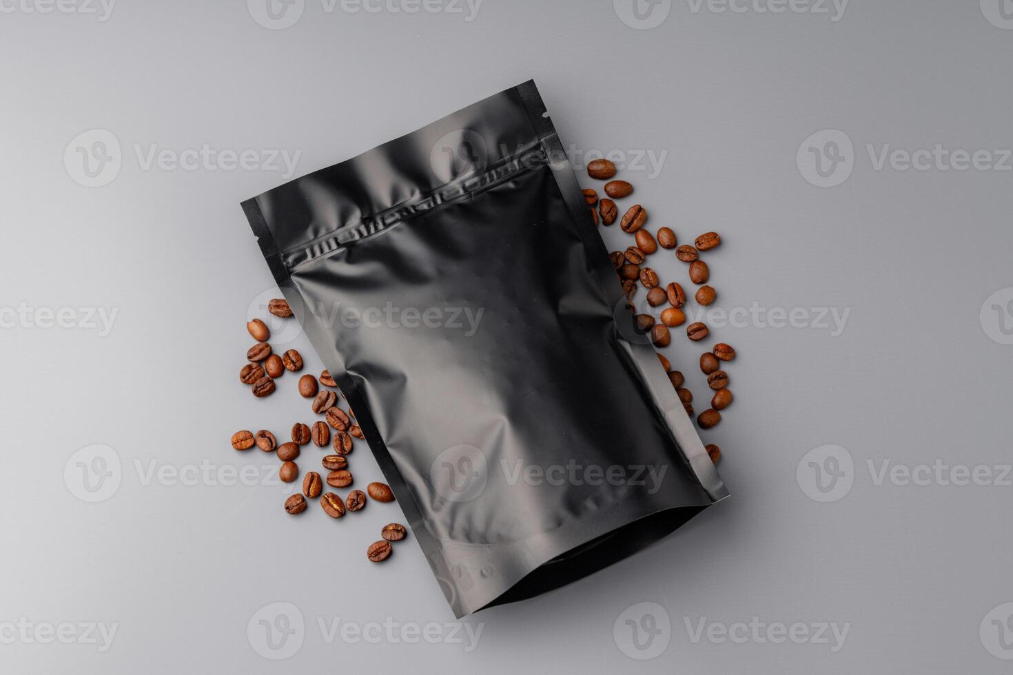 A bag of premium coffee beans surrounded by scattered coffee beans on a gray background photo