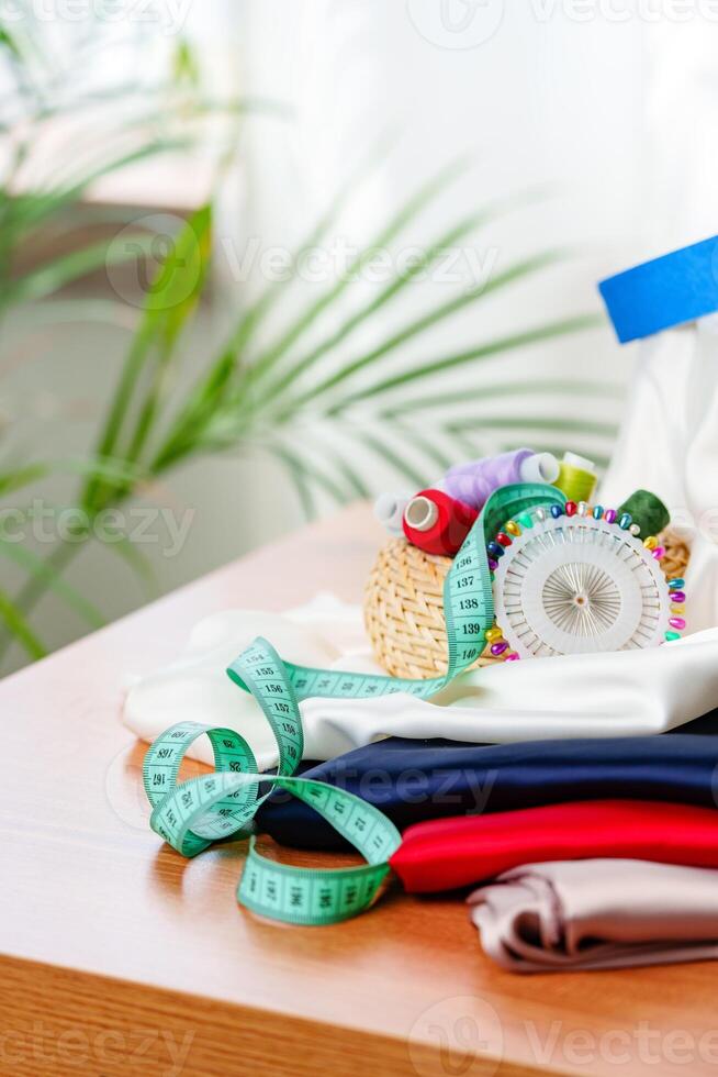 Crafting supplies arranged on a wooden table with colorful threads, measuring tape, and fabric in a well-lit workspace photo